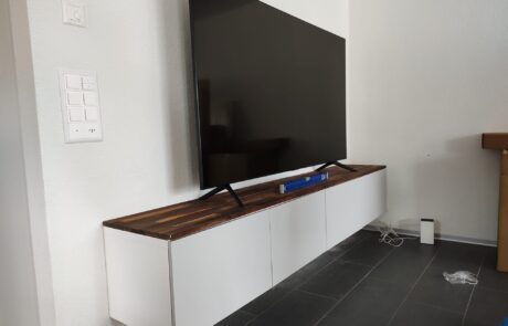 Wandmontierter Fernseher über einem weissen TV-Möbel mit Holzabdeckung